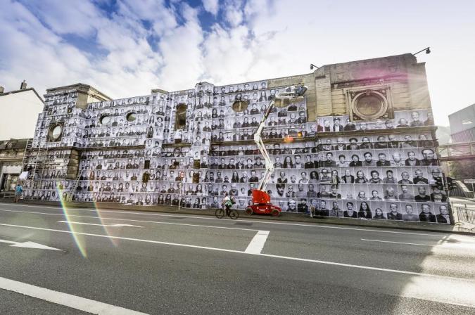 A large wall beside the city streets features an art exhibit of portraits from the Inside Out Project.